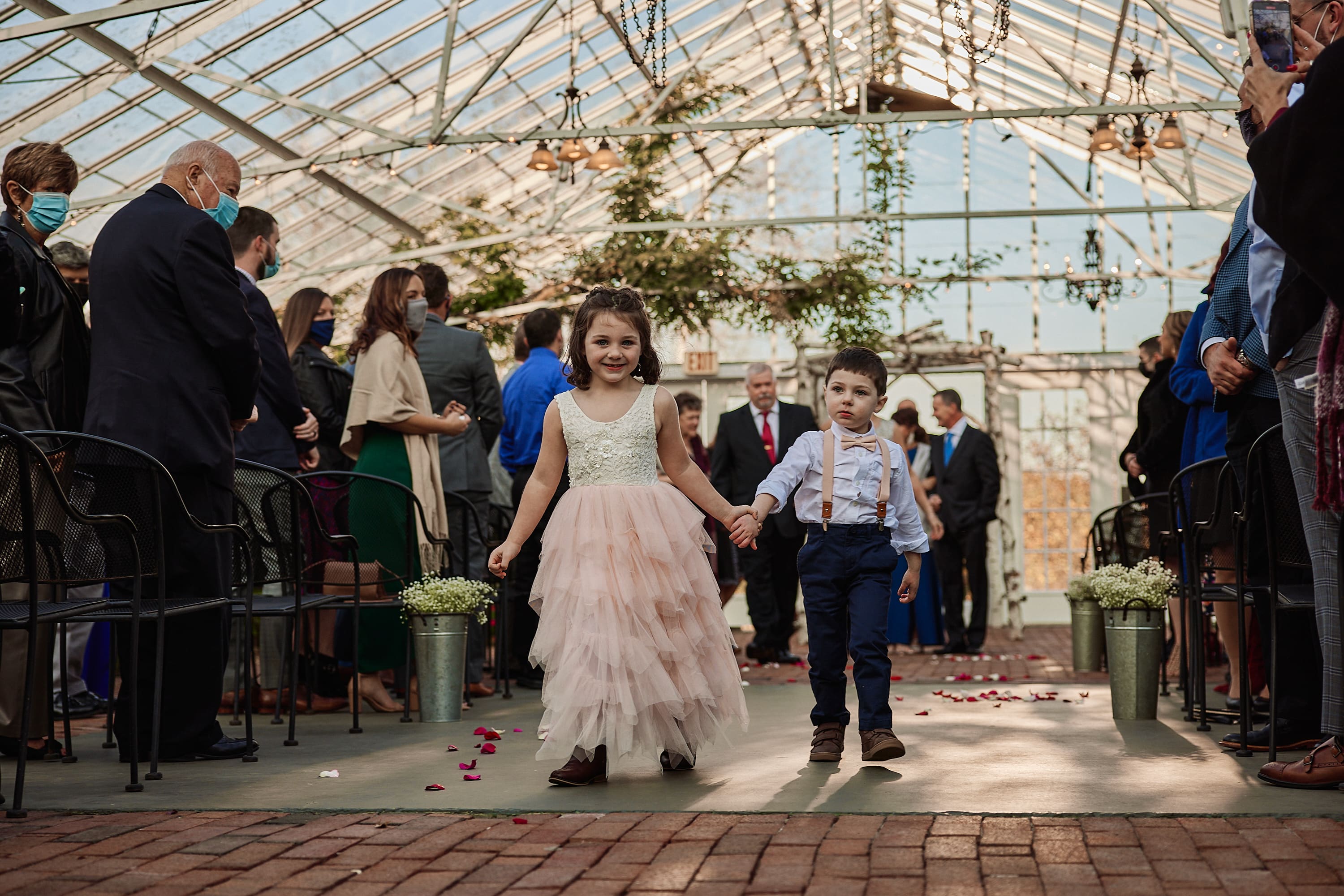 Candid wedding photo of a flower girl walking down the aisle in a greenhouse